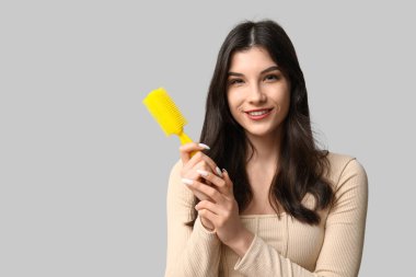 Gri arkaplanda sarı saç fırçası olan güzel bir genç kadın.