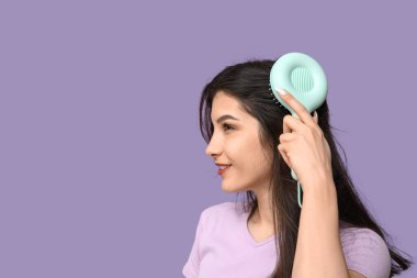 Saçlarını leylak arka planda tarayan güzel genç bir kadın.