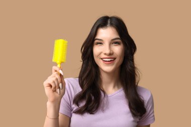 Kahverengi arka planda sarı saç fırçası olan güzel bir genç kadın.