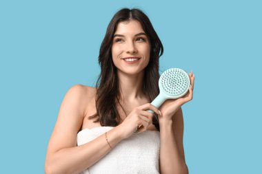 Mavi arka planda saç fırçası olan güzel genç bir kadın.