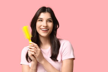 Pembe arka planda sarı saç fırçası olan güzel bir genç kadın.