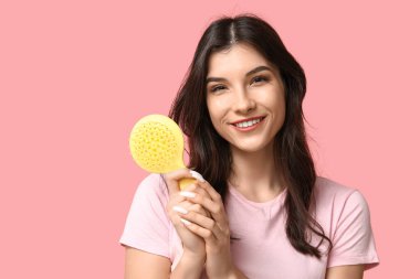 Pembe arka planda sarı saç fırçası olan güzel bir genç kadın.