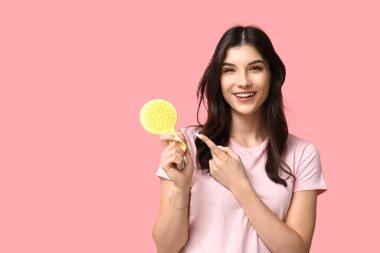 Pembe arka planda sarı saç fırçasını gösteren güzel bir genç kadın.