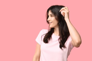 Güzel genç bir kadın pembe arka planda saçını tarıyor.