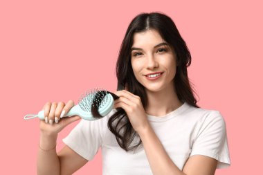 Güzel genç bir kadın pembe arka planda saçını tarıyor.