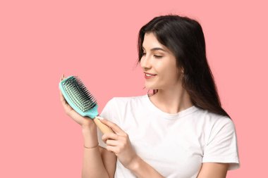 Pembe arka planda turkuaz saç fırçası olan güzel bir genç kadın.