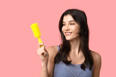 Pembe arka planda sarı saç fırçası olan güzel bir genç kadın.