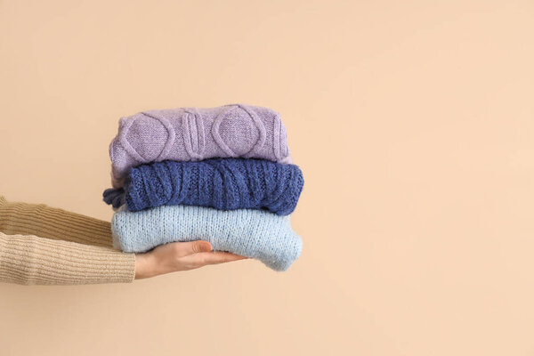 Женщина со сложенными свитерами на бежевом фоне