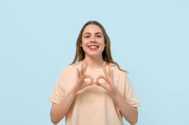 Young deaf mute woman using sign language on blue background
