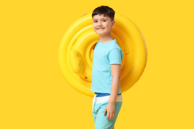 Sarı arka planda şişirilebilir yüzüğü olan sevimli küçük bir çocuk.