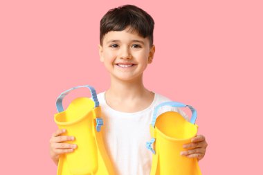 Pembe arka planda sarı paletleri olan sevimli küçük bir çocuk.