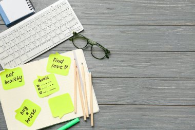 Yapılacaklar listesi, bilgisayar klavyesi ve siyah tahta zemin üzerine not defteri olan yapışkan notlar. Yeni yıl hedefleri kavramı