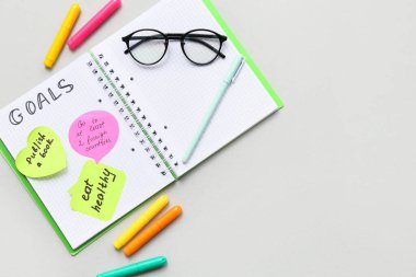 Planı olan bir defter, gri arka planda yapışkan notlar ve kırtasiye malzemesi. Yeni yıl hedefleri kavramı