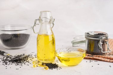 Beyaz arka planda susam tohumlu bir şişe ve bir kase yağ.