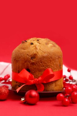 Lezzetli Panettone tabağı ve kırmızı arka planda Noel dekoru.