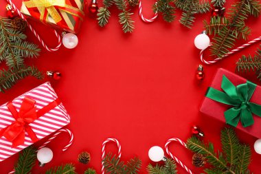 Noel hediyesi kutuları, toplar, köknar ağacı dalları ve kırmızı arka planda şeker kamışı oyuncaklarından yapılmış çerçeve