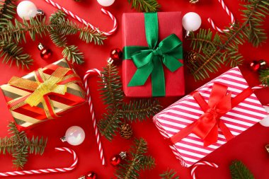 Toplu Noel hediyesi kutuları, köknar ağacı dalları ve kırmızı arka planda şeker kamışı oyuncakları