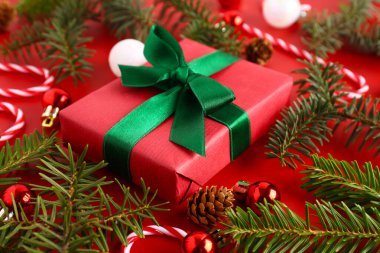 İçinde toplar, köknar ağacı dalları ve kırmızı arka planda şeker kamışı oyuncakları olan Noel hediyesi kutusu.