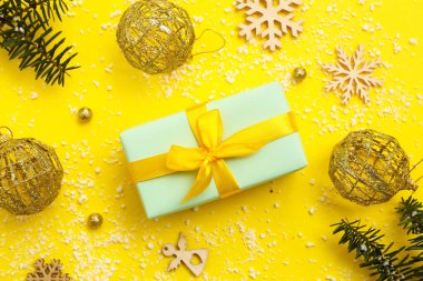 Noel hediyesi kutusu, köknar dalları, toplar ve sarı arka planda tahta kar taneleri.