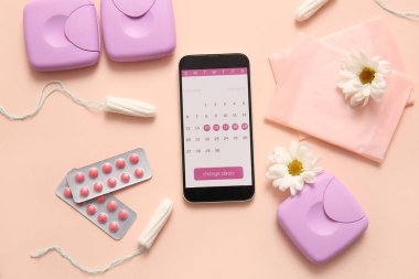 Cep telefonu ekranında adet takvimi ve bej arka planda kadın hijyen ürünleri