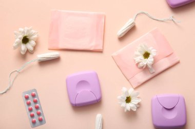 Tamponlu regl pedleri, depolama kutuları, papatya çiçekleri ve bej arka planda haplar.