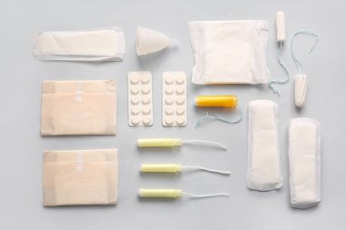 Regl pedi, tampon, fincan ve gri arka planda haplar.