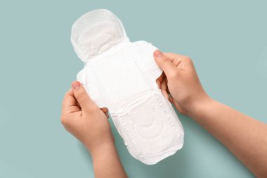 Mavi arka planda adet pedi olan kadın eller.