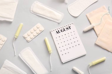 Regl takvimi, tamponlar ve gri arka planda haplar.