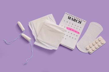 Adet takvimi, tamponlar ve mor arka planda haplar.