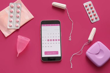 Cep telefonu ekranında adet takvimi ve renk arka planında kadın hijyen ürünleri