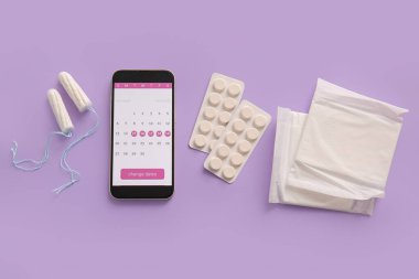 Cep telefonu ekranında adet takvimi ve mor arka planda kadın hijyen ürünleri