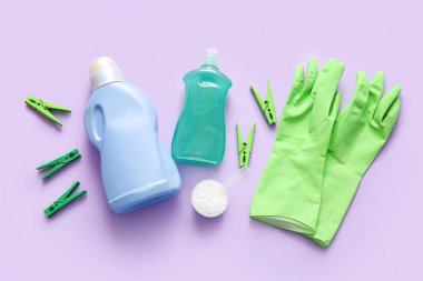 Çamaşır deterjanı, mandallar ve mor arka planda lastik eldivenler.