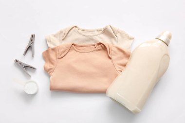 Çamaşır deterjanı, mandallar ve beyaz arka planda bebek kıyafetleri.