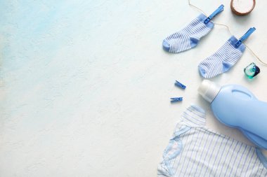 Çamaşır deterjanları, çamaşır mandalları, bebek tulumu ve arka planda çoraplar.