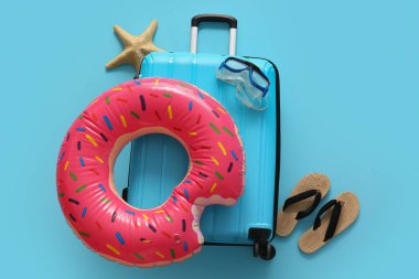 Şişirilebilir yüzüklü bavul, parmak arası terlik, deniz yıldızı ve mavi arka planda yüzme maskesi.