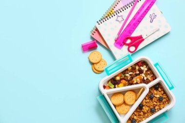 Lezzetli yemeklerle beslenme çantası ve mavi arka planda okul kırtasiyesi.