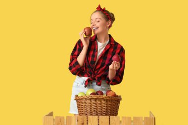 Sarı arka planda elma sepeti olan genç bir kadın.