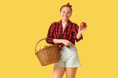 Sarı arka planda elma sepeti olan genç bir kadın.