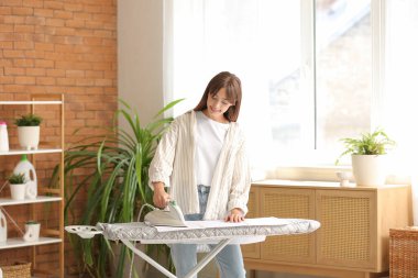 Çamaşır odasında havlu ütüleyen genç bir kadın.