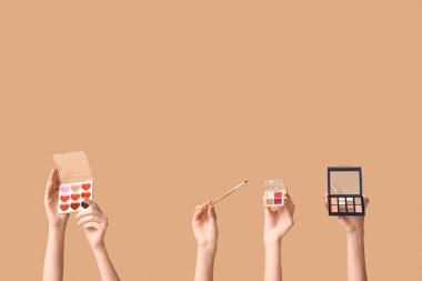 Farklı göz falı paletleri olan kadın elleri ve kahverengi arka planda makyaj fırçası.