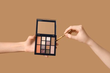 Göz falı paleti ve kahverengi arka planda makyaj fırçası olan kadın elleri