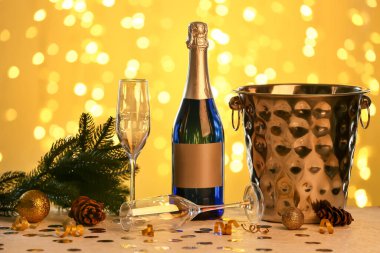 Bulanık ışıklara karşı şampanya, bardak ve Noel dekoruyla dolu buz kovası.