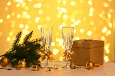 Noel ağacı dallı şampanya bardakları, bulanık ışıklara karşı hediye kutusu ve toplar.