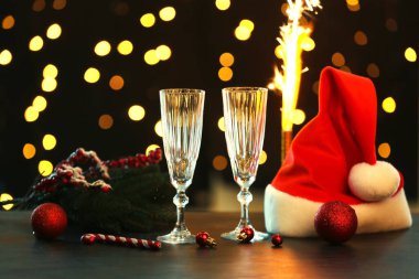 Bulanık ışıklara karşı Noel Baba şapkalı ve Noel dekorlu şampanya bardakları.