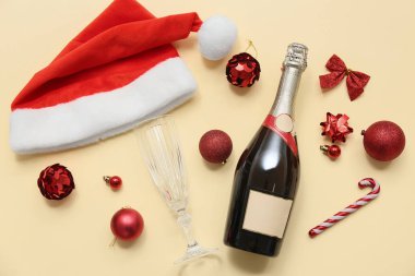 Cam kaplı bir şişe şampanya, Noel Baba şapkası ve sarı arka planda Noel dekoru.