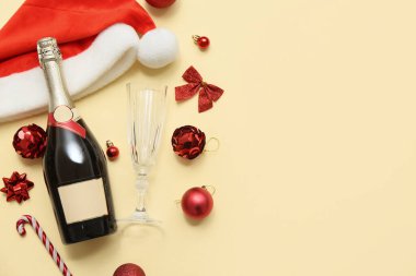 Cam kaplı bir şişe şampanya, Noel Baba şapkası ve sarı arka planda Noel dekoru.