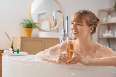 Bir bardak şampanyası olan genç bir kadın evde banyo yapıyor.
