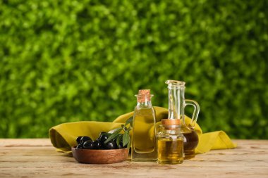 Dekan ve taze zeytinyağı şişeleri dışarıda, ahşap masada.