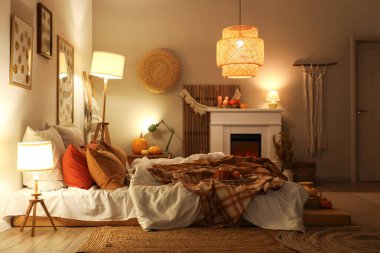 Şık yatak odasının içinde sonbahar süslemeleri ve şöminede mumlar var.