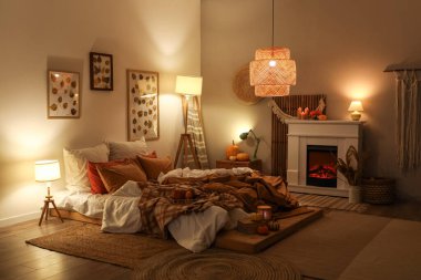 Şık yatak odasının içinde sonbahar süslemeleri ve şöminede mumlar var.